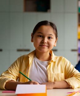 A young girl smiling while writing at her desk